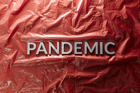 pandemic 这个词在红色皱巴巴的塑料薄膜背景上用银色字母放置在中心的平躺组合中