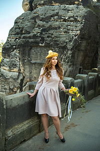 在瑞士萨克森、德国、巴斯泰的山脉和峡谷背景中，一个穿着粉色裙子和一顶带花束的帽子的女孩