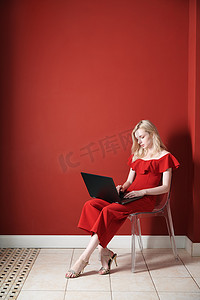 便携式椅子摄影照片_坐在椅子上并在笔记本电脑上工作的年轻成年女性