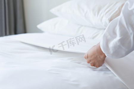 客房女服务员摄影照片_女手在卧室里铺上白色床单