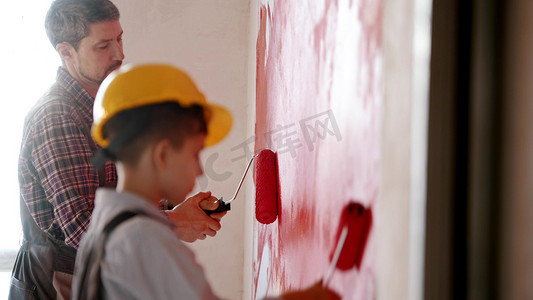 一个小男孩和他的父亲用红色粉刷墙壁 — 一个戴着头盔的男孩
