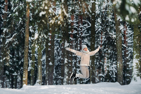 一个穿着灰色衣服的女人在冬季森林里情绪激动地跳跃。新年白雪覆盖的森林里的女孩。