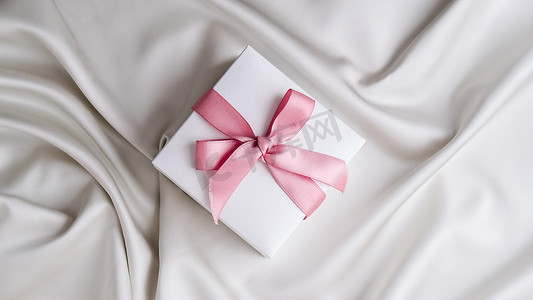 白色织物丝绸背景上有粉红丝带的礼品盒。