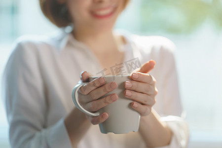 在早晨的阳光下，女人手拿着一杯热咖啡或茶