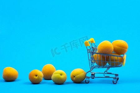 蓝色背景上装有杏子的购物篮。购物车