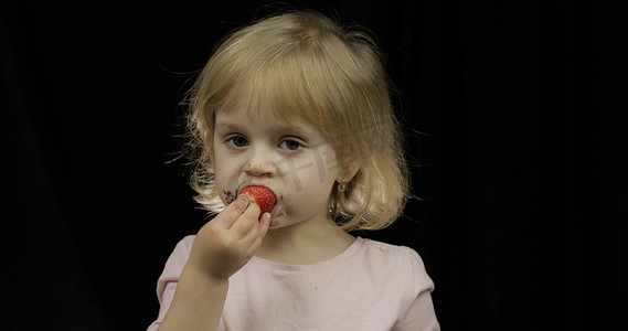 脏脸摄影照片_融化的巧克力和生奶油弄脏脸的孩子吃草莓