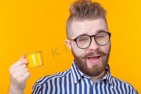 一个有趣自信的英俊年轻人的画像，他戴着眼镜，留着胡子，黄色背景上有一个黄色的小杯子。