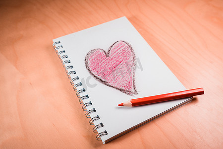 红色的笔摄影照片_笔记本上的爱心，橙色木桌上的笔