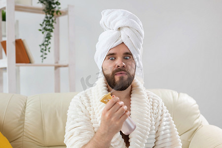 留着胡须的男性头上戴着浴巾，在脸上喷水处理。