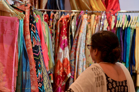 印度新德里 Dilli Haat 或 Sarojini nagar 市场的一家商店里，一位戴着眼镜的印度老妇正在检查设计师 kurta (Salwar Kamiz)