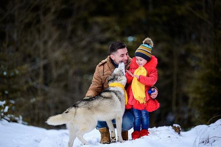 快乐的父亲带着女儿和他们的宠物在冬季公园里遛狗。
