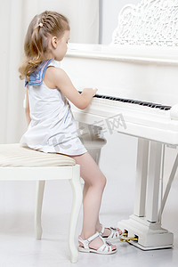 美丽的小女孩正在一架白色三角钢琴上弹奏。
