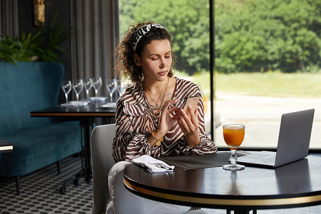 鲜橙咖啡摄影照片_坐在咖啡馆里喝鲜橙汁等朋友的卷发美女