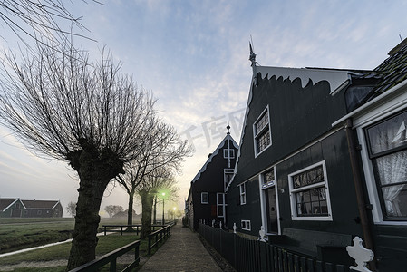 城市建筑矢量摄影照片_悬挂的灯柱美丽的典型荷兰木屋建筑在日出时刻反映在位于荷兰阿姆斯特丹北部的 Zaanse Schans 平静的运河上