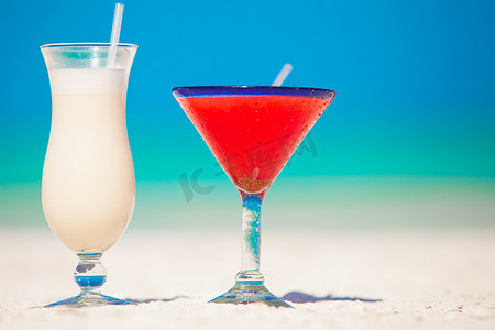 两杯鸡尾酒：白色沙滩上的冰镇果汁朗姆酒和草莓玛格丽塔