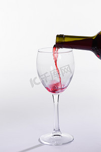 解百纳摄影照片_红酒从瓶子里倒入白色背景中的大玻璃杯