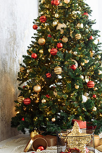 温暖的房间摄影照片_在明亮的房间里，圣诞树上挂着红色和金色的球，还有金色的花环灯。