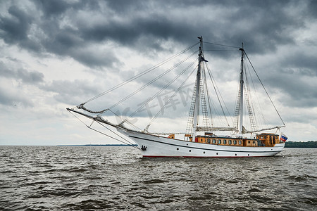 霜降下霜摄影照片_白色古董帆船护卫舰出海，暴风雨天空降低，风帆降下，桅杆和绳索