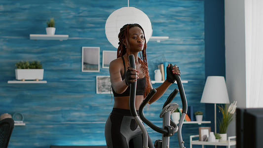 适合运动的黑人女性在椭圆自行车上跑步观看健康常规
