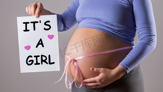 孕妇肚子上挂着粉色丝带的纸，上面写着是女孩