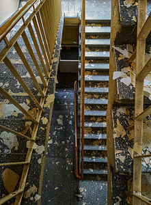 从上到下看带有金属栏杆的混凝土楼梯和从旧废弃医院墙上剥落的画作