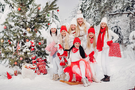 白雪皑皑的森林摄影照片_一大群女孩手里拿着圣诞礼物站在冬天的森林里。穿着红白相间衣服的女孩在白雪皑皑的森林里拿着圣诞礼物