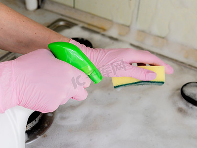 一位戴着粉色手套的女士用毛巾和清洁剂清洗煤气灶。