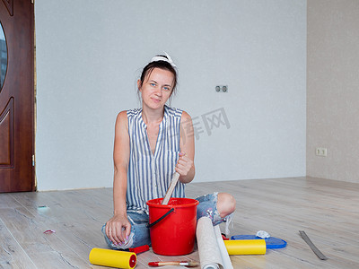 一名妇女坐在地板上，在红色桶中混合胶水，用于在公寓里贴壁纸。