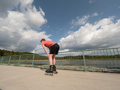 身穿红色 T 恤、带直排轮滑鞋的中年男子在夏季公园、流行的户外滑冰场上骑行。