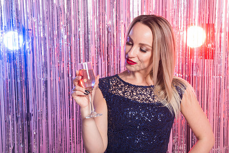 派对、饮料、节日和庆祝概念 — 穿着晚礼服的微笑女人，在闪亮的背景下喝着一杯起泡酒。