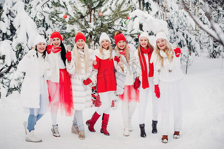 在红雪摄影照片_一大群手里拿着香槟酒的女孩站在冬天的森林里。穿着红白相间衣服的女孩在白雪覆盖的森林里喝着新年的饮料。