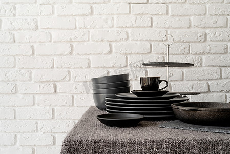 白色砖墙背景的桌子上堆放着黑色陶瓷盘子和餐具