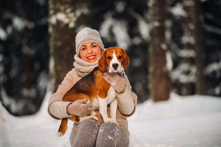 一个冬日的女人和她的宠物狗小猎犬在冬天的森林里玩耍