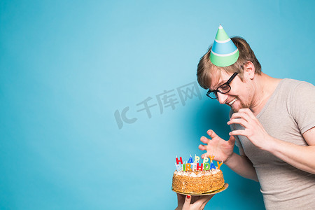 戴着问候纸帽的滑稽疯狂年轻人想咬掉一块祝贺蛋糕。