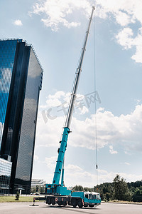 最高和最大的蓝色汽车起重机被放置在一座大型现代建筑旁边的平台上。
