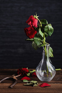枯萎的摄影照片_深灰色背景上枯萎的玫瑰和带落花瓣和落叶的木桌，悲伤情人节浪漫的设计理念，破碎，复制，空间。