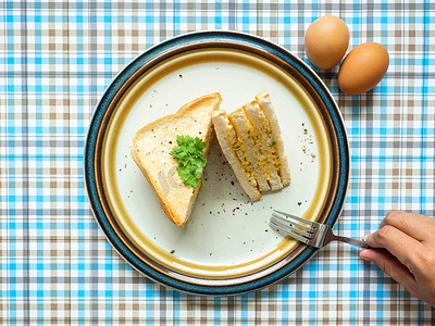 鸡蛋三明治、配料鸡蛋、盐、胡椒和面包放在白盘上，用叉子吃，蓝色背景，用作墙纸
