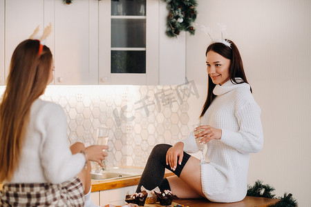 两个女孩在厨房里享受舒适的家庭环境，手里拿着香槟庆祝圣诞节。