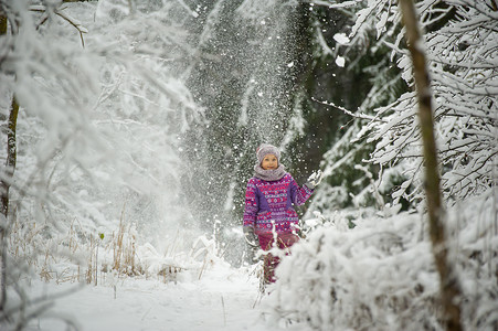 一个冬天穿着紫色衣服的小女孩穿过白雪覆盖的森林