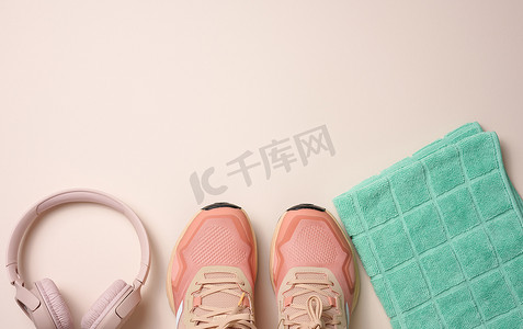 一双粉色纺织运动鞋、无线耳机和一条米色背景的绿色纺织毛巾。