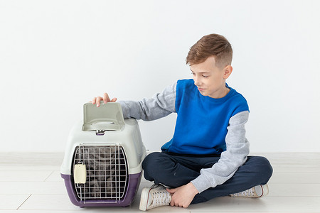 小男孩拿摄影照片_笑着的积极的小男孩拿着一个笼子，旁边是一只苏格兰折叠猫，坐在新公寓的地板上。