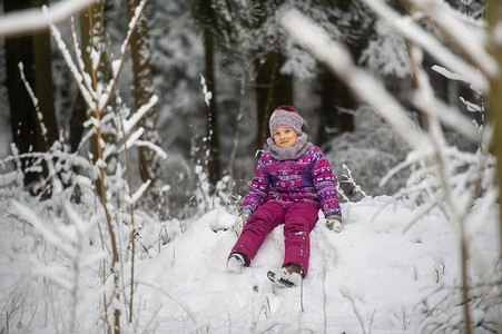 紫色衣服摄影照片_一个冬天穿着紫色衣服的小女孩穿过白雪覆盖的森林
