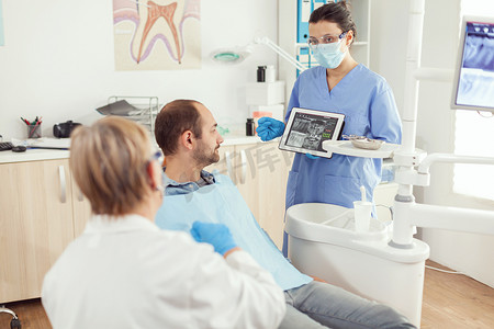 放射线摄影照片_牙科诊所的口腔护士展示带有牙齿放射线照相的平板电脑