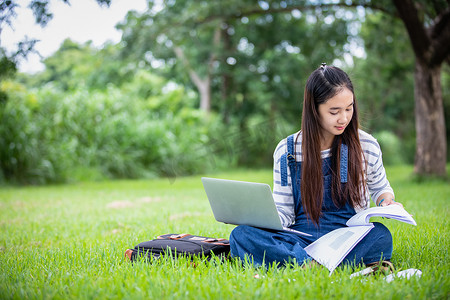 美丽的亚洲女学生拿着书，对着镜头微笑，夏天在公园里学习和教育理念，放松时间