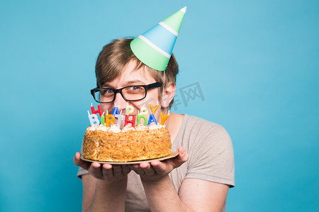 海报祝贺摄影照片_戴着问候纸帽的滑稽疯狂年轻人想咬掉一块祝贺蛋糕。