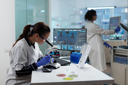 专业生物学家研究员使用医学显微镜分析生物医学病毒样本