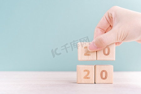 摘要 2020 年和 2019 年新年倒计时设计理念 — 女性在木桌和绿色背景上拿着木块立方体，特写，复制空间。
