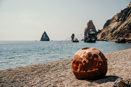 矿山背景摄影照片_旧生锈的圆形浮动海洋地雷在海滩上有岩石海岸和海洋背景。