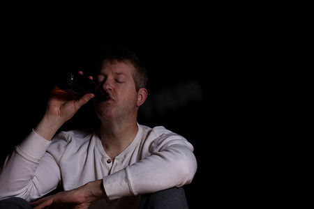 喝啤酒摄影照片_黑暗背景中喝啤酒的抑郁成熟男人