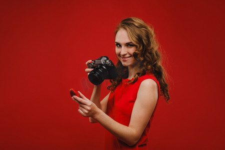 一位微笑的年轻女子，一头波浪形的头发，拿着草莓并拍照，在鲜红色背景上拿着美味的新鲜草莓